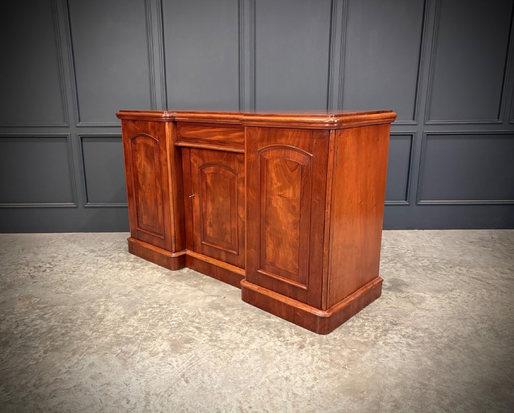 A Victorian mahogany three-door sideboard featuring flame mahogany panelled cupboard doors and a central top drawer on a solid plinth base. View IX