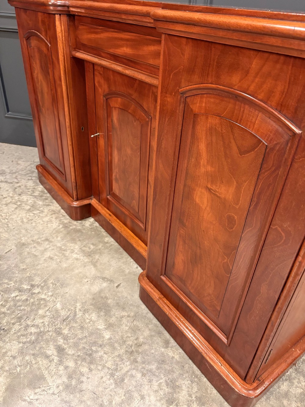 A Victorian mahogany three-door sideboard featuring flame mahogany panelled cupboard doors and a central top drawer on a solid plinth base. View X