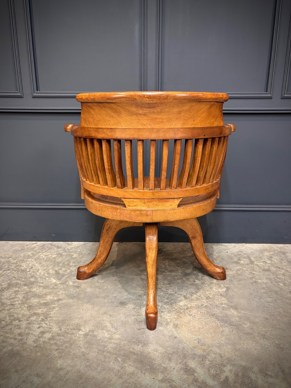 A light mahogany swivel desk chair featuring a curved slatted backrest, sweeping armrests, a shaped solid wooden seat, and a four-legged revolving base. View VIII