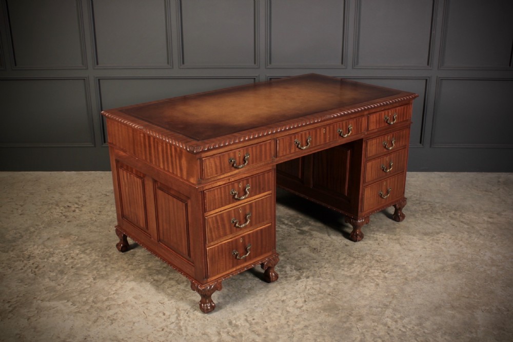 A mahogany pedestal desk with a brown leather inset writing surface, swan-neck brass handles, and carved claw and ball feet.