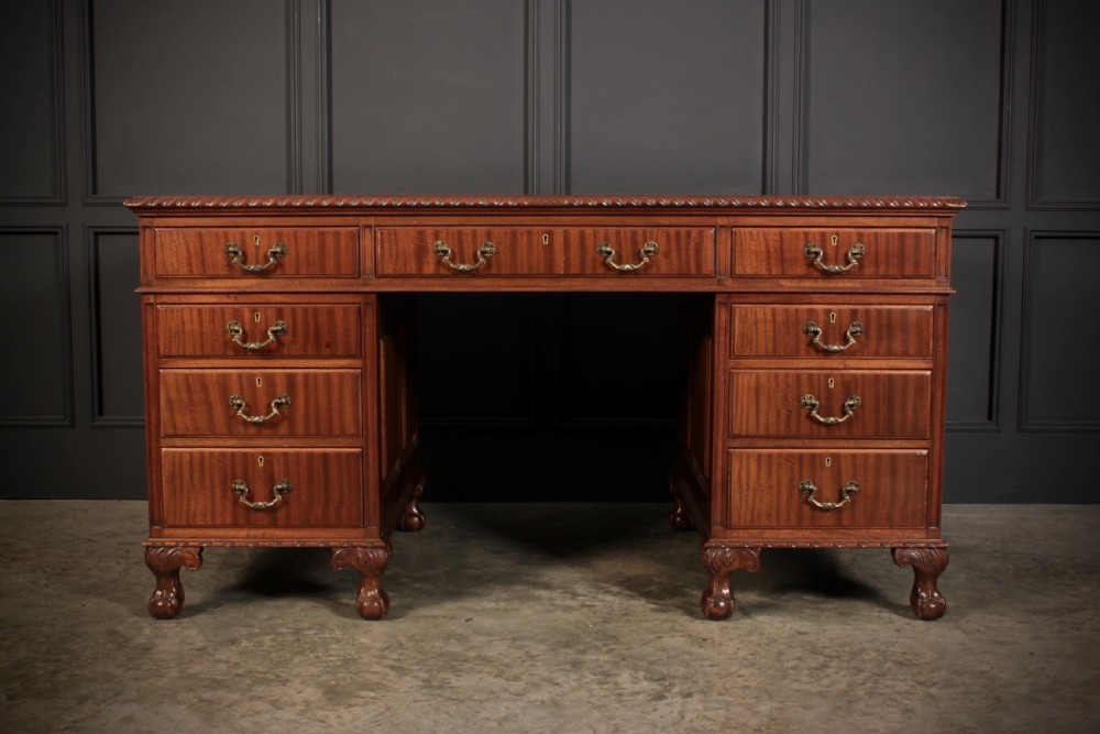 A mahogany pedestal desk with a brown leather inset writing surface, swan-neck brass handles, and carved claw and ball feet. View V