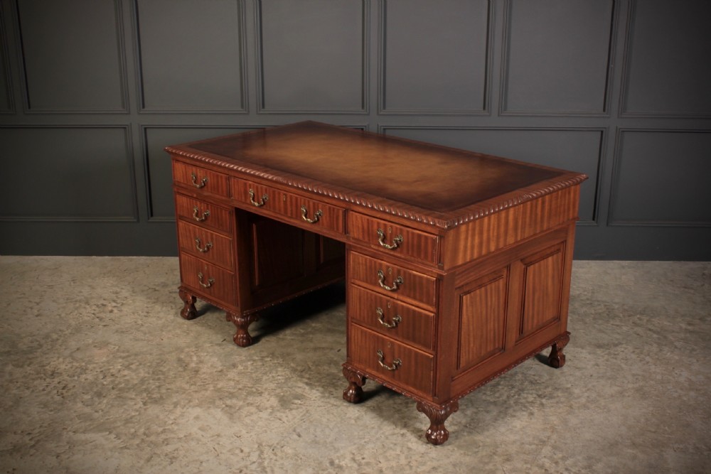 A mahogany pedestal desk with a brown leather inset writing surface, swan-neck brass handles, and carved claw and ball feet. View VI