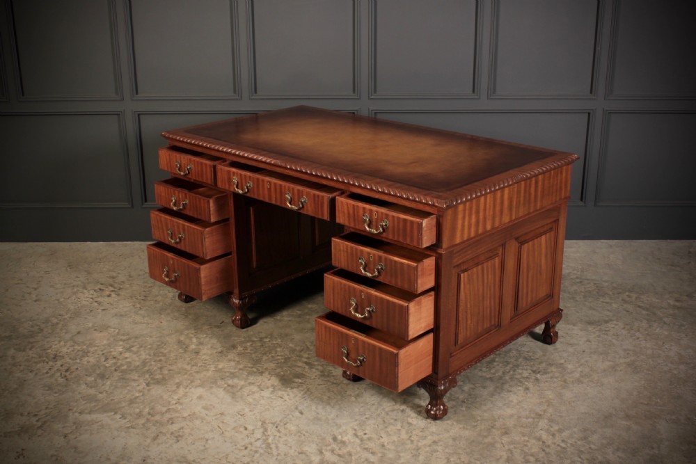 A mahogany pedestal desk with a brown leather inset writing surface, swan-neck brass handles, and carved claw and ball feet. View VII