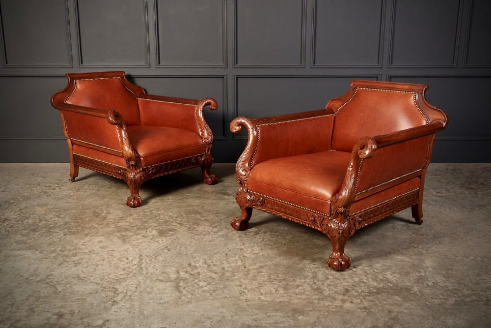 A pair of carved mahogany armchairs upholstered in warm chestnut brown leather with brass stud detailing and ornate scroll arms. View II