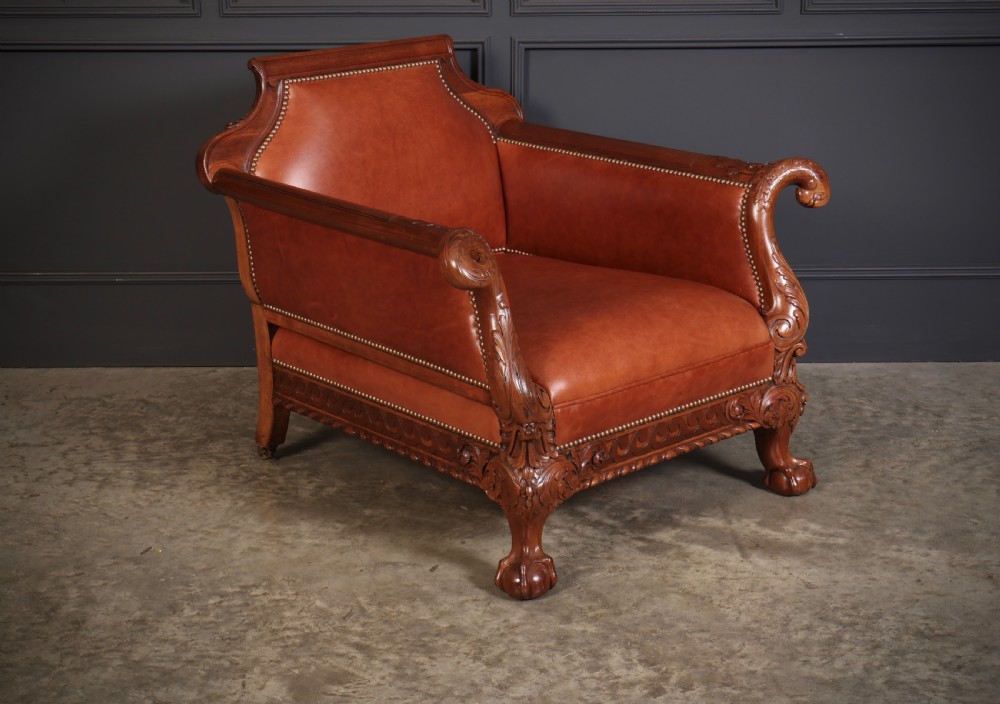 A pair of carved mahogany armchairs upholstered in warm chestnut brown leather with brass stud detailing and ornate scroll arms. View III