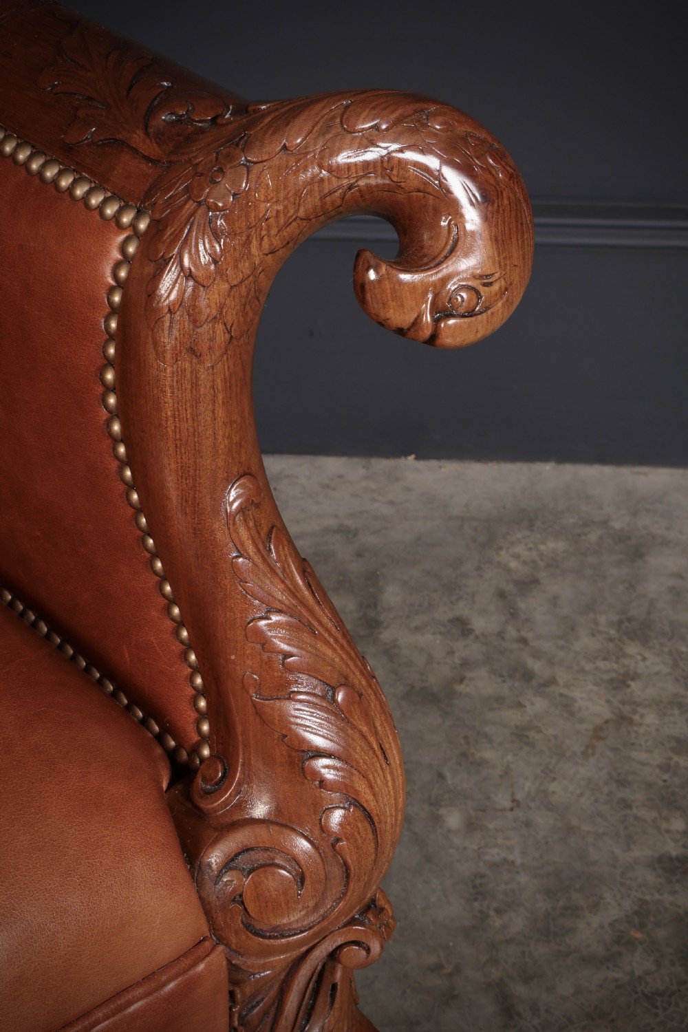 A pair of carved mahogany armchairs upholstered in warm chestnut brown leather with brass stud detailing and ornate scroll arms. View IV