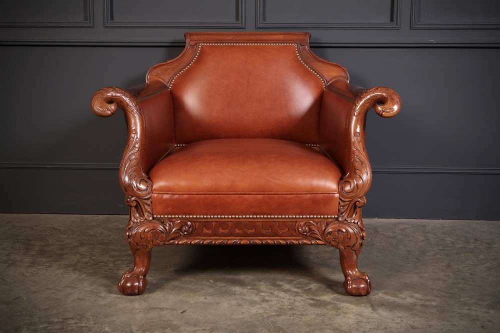 A pair of carved mahogany armchairs upholstered in warm chestnut brown leather with brass stud detailing and ornate scroll arms. View VI