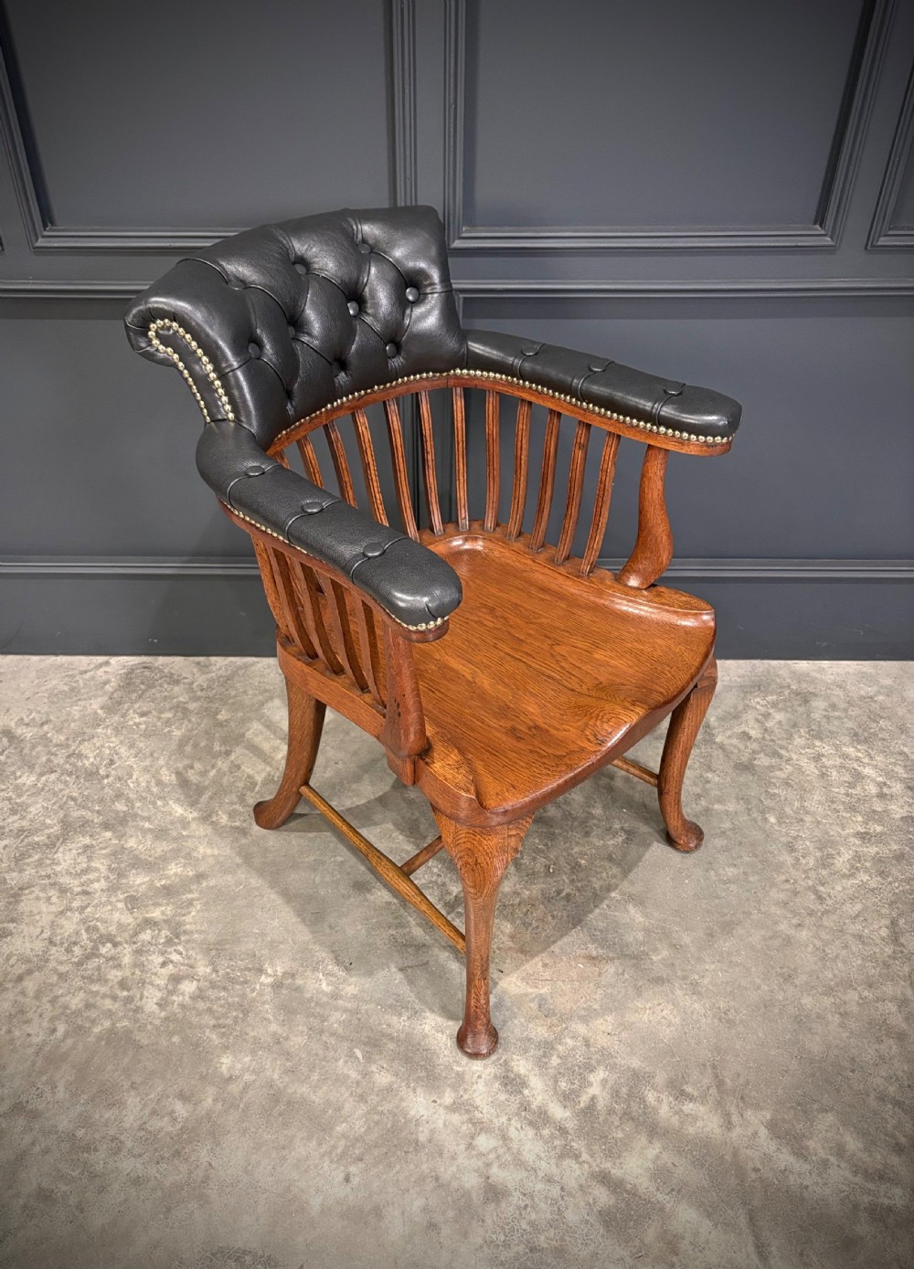 A Victorian oak desk chair featuring a deep-buttoned black leather top rail with brass studs, an open spindle back, shaped wooden seat, and cabriole front legs. View II