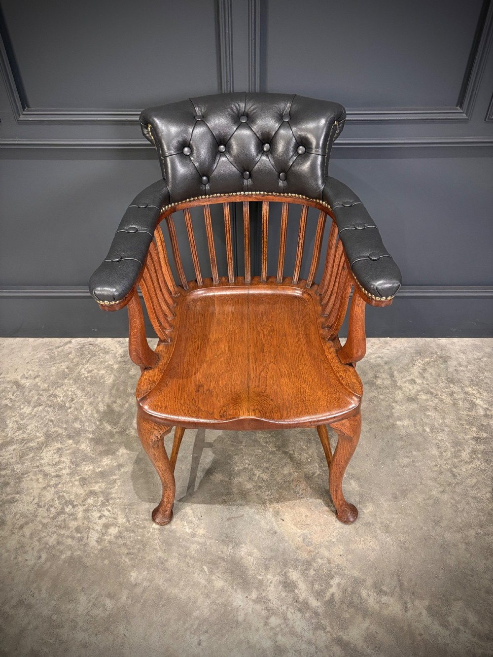 A Victorian oak desk chair featuring a deep-buttoned black leather top rail with brass studs, an open spindle back, shaped wooden seat, and cabriole front legs. View III