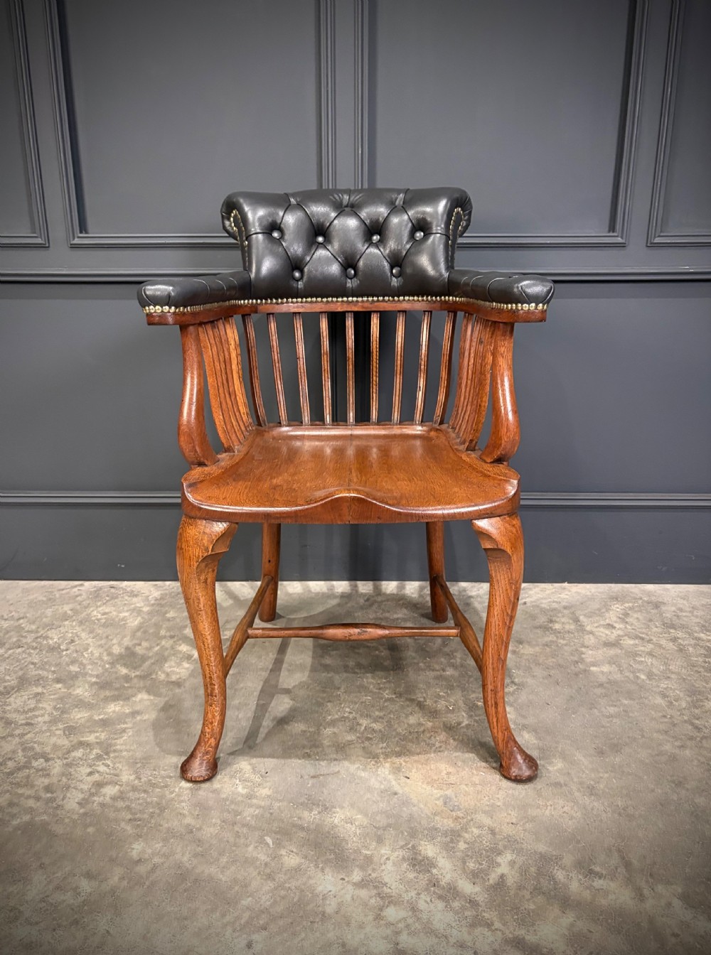 A Victorian oak desk chair featuring a deep-buttoned black leather top rail with brass studs, an open spindle back, shaped wooden seat, and cabriole front legs. View IV