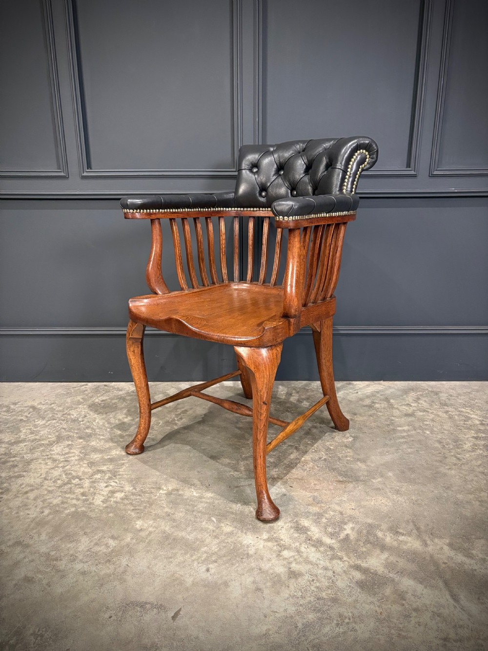 A Victorian oak desk chair featuring a deep-buttoned black leather top rail with brass studs, an open spindle back, shaped wooden seat, and cabriole front legs. View V