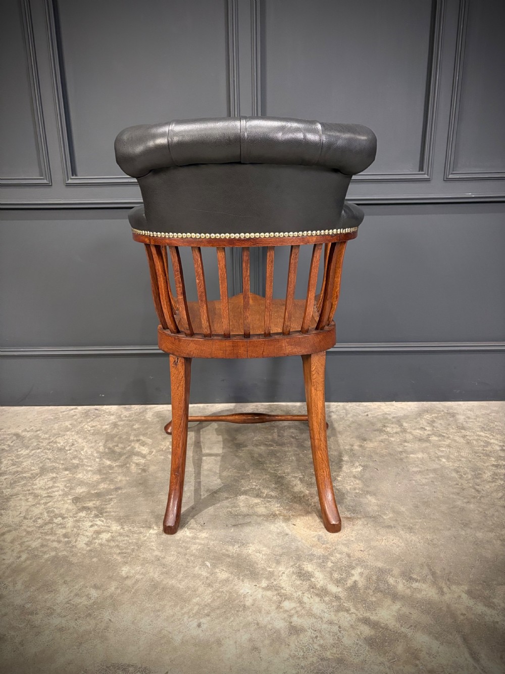 A Victorian oak desk chair featuring a deep-buttoned black leather top rail with brass studs, an open spindle back, shaped wooden seat, and cabriole front legs. View VIII
