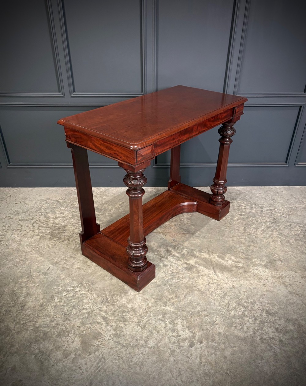 An antique dark mahogany console table featuring carved turned columns and a solid plinth base.