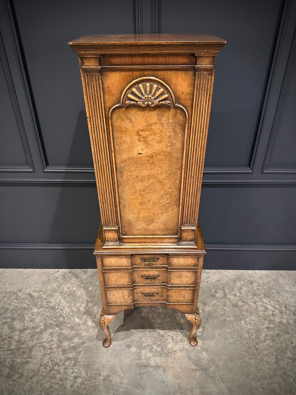 A tall, narrow Queen Anne style walnut bookcase featuring an arched burr walnut front panel, open side shelving, three drawers with brass handles, and cabriole legs with carved shell knees. View IV