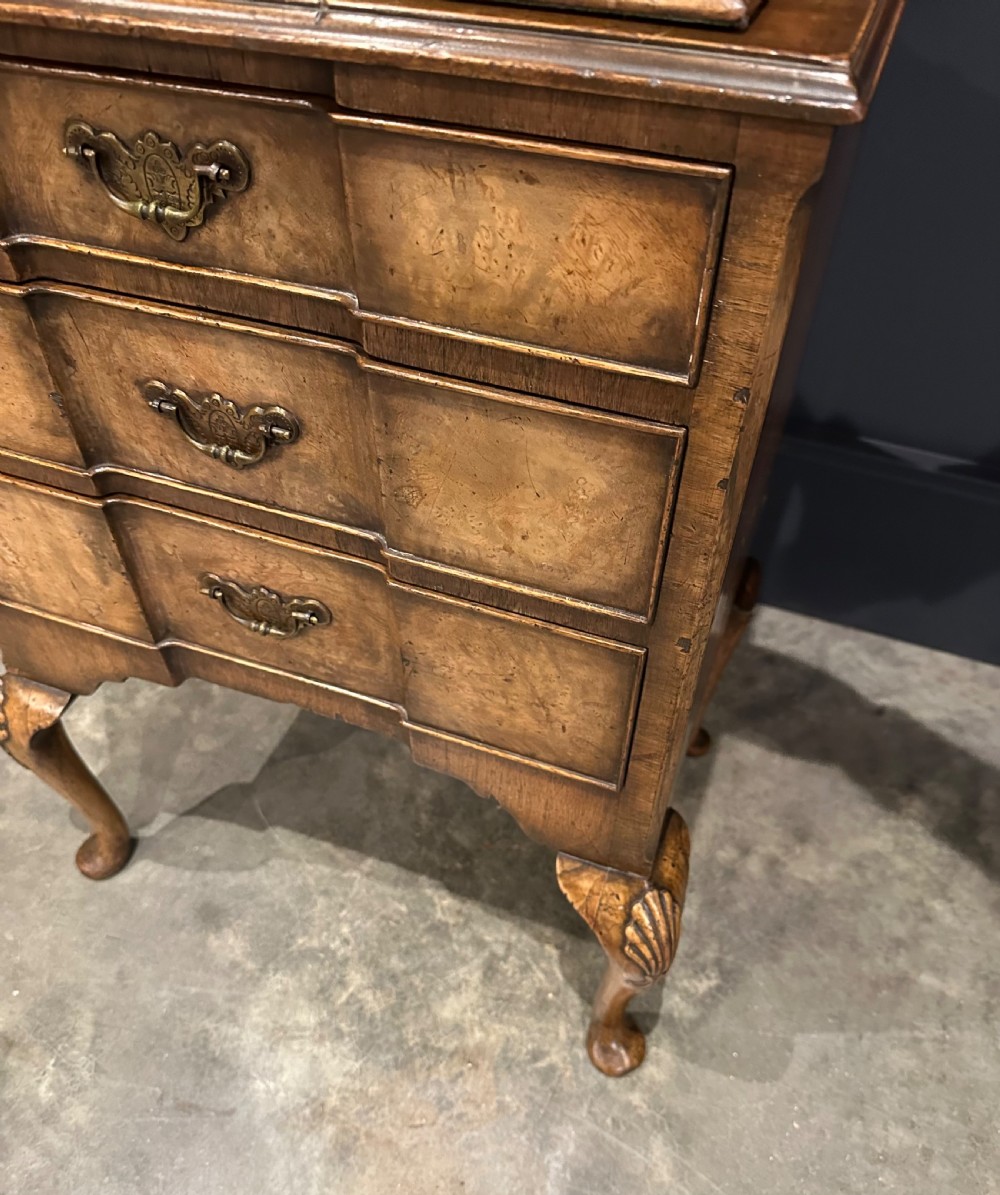 A tall, narrow Queen Anne style walnut bookcase featuring an arched burr walnut front panel, open side shelving, three drawers with brass handles, and cabriole legs with carved shell knees. View V