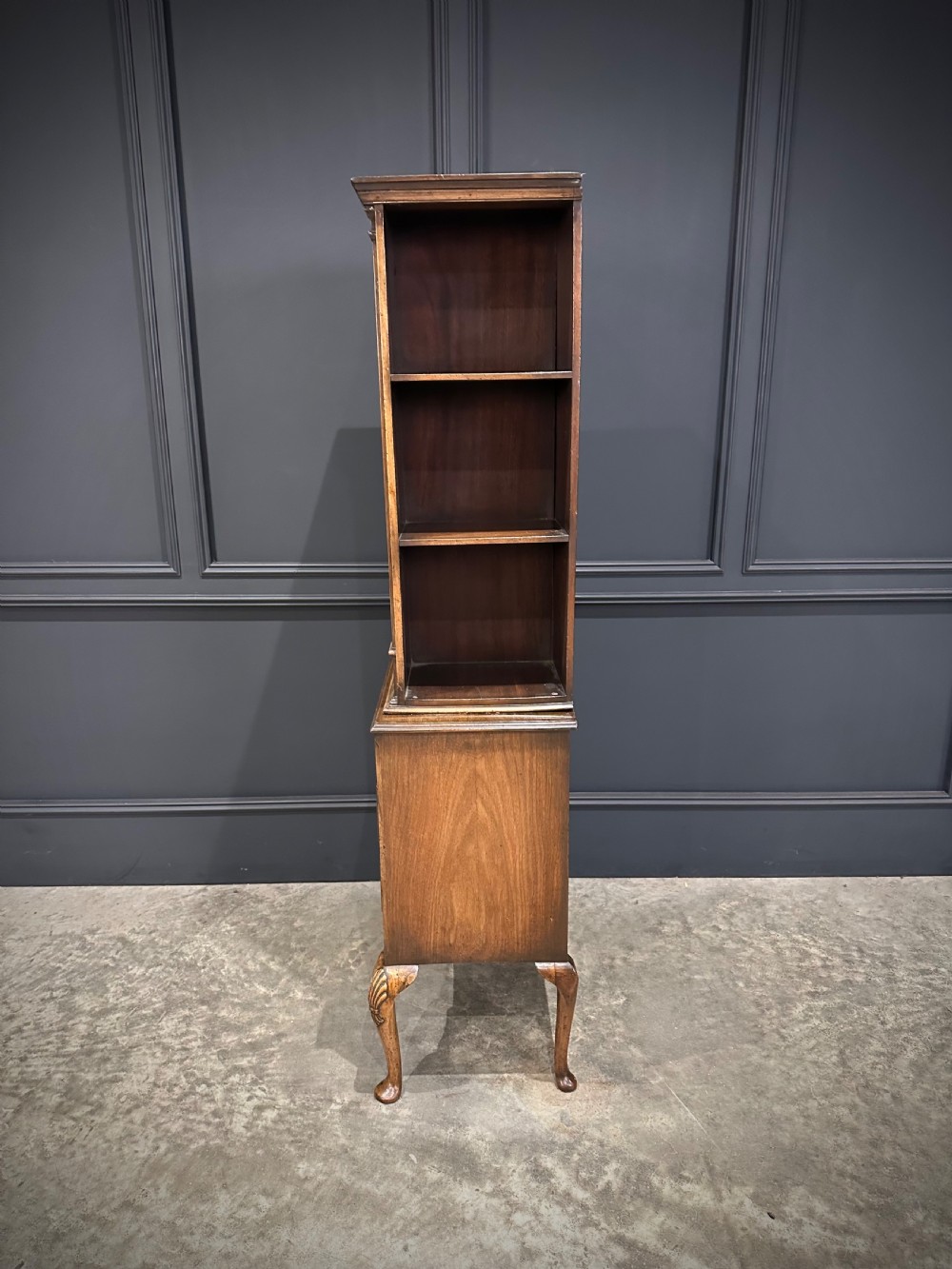 A tall, narrow Queen Anne style walnut bookcase featuring an arched burr walnut front panel, open side shelving, three drawers with brass handles, and cabriole legs with carved shell knees. View XII