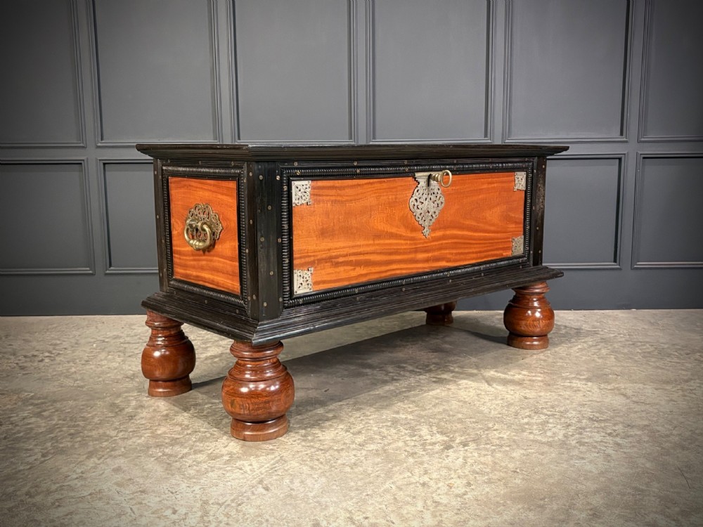 A large Ceylonese camphor wood and ebony storage trunk with an ornate metal escutcheon, side handles, and heavy turned bulbous feet.