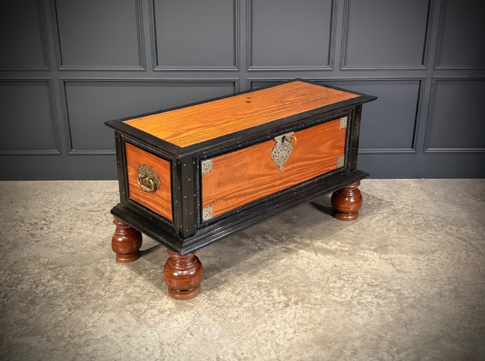 A large Ceylonese camphor wood and ebony storage trunk with an ornate metal escutcheon, side handles, and heavy turned bulbous feet. View II