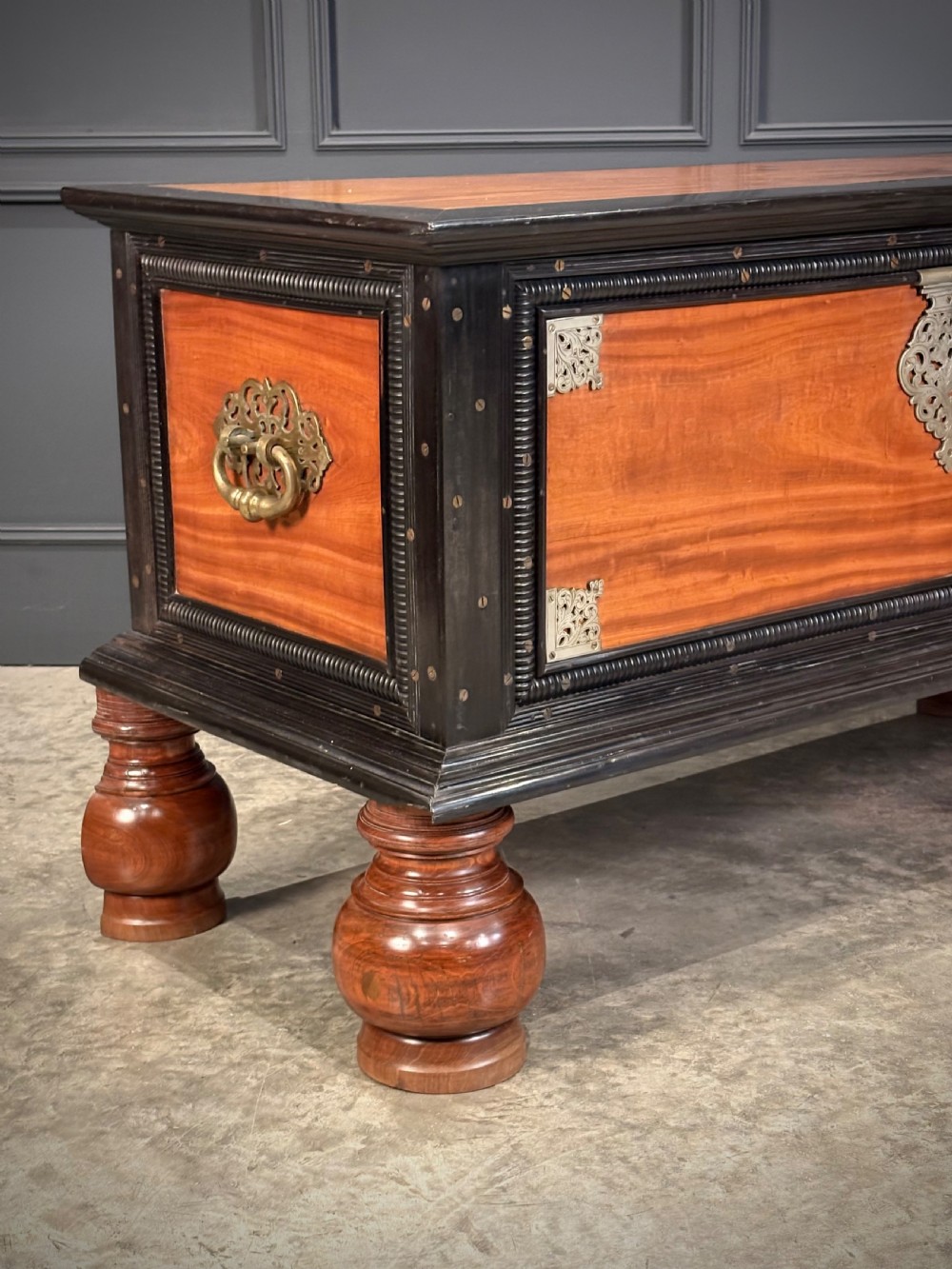 A large Ceylonese camphor wood and ebony storage trunk with an ornate metal escutcheon, side handles, and heavy turned bulbous feet. View III