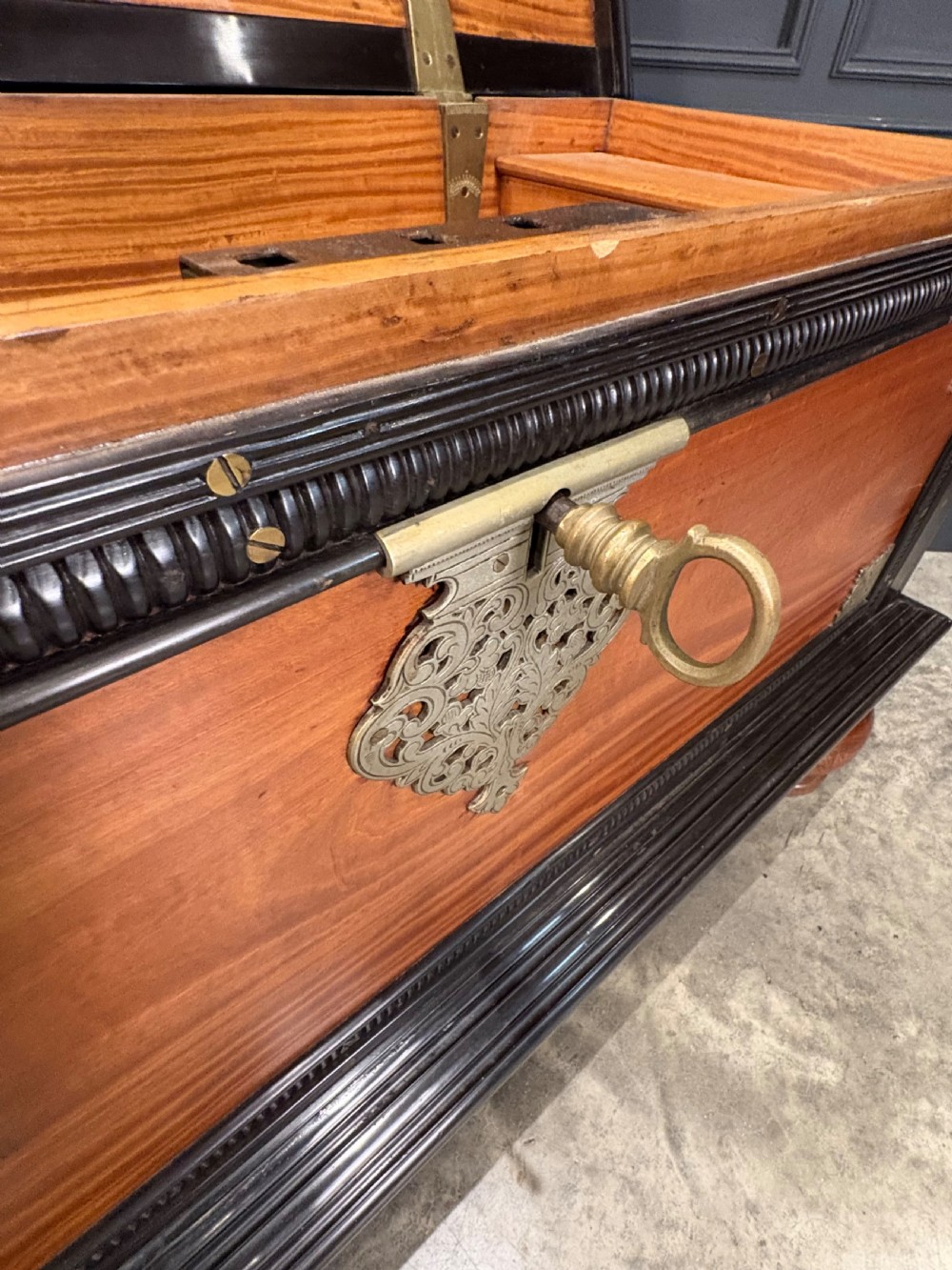 A large Ceylonese camphor wood and ebony storage trunk with an ornate metal escutcheon, side handles, and heavy turned bulbous feet. View VI