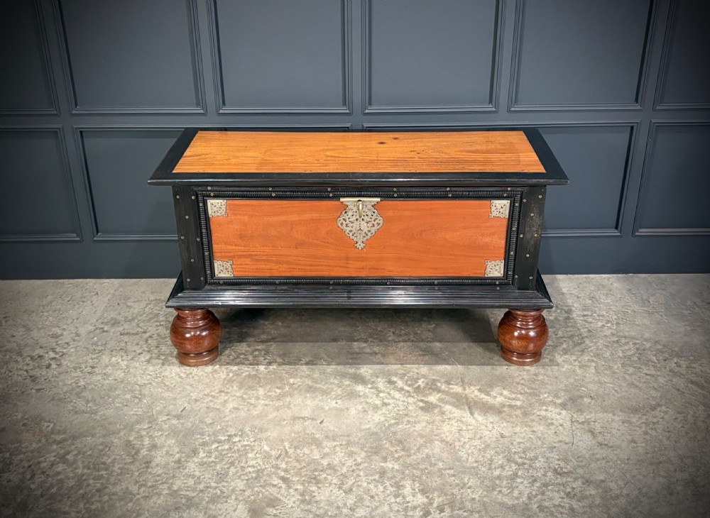 A large Ceylonese camphor wood and ebony storage trunk with an ornate metal escutcheon, side handles, and heavy turned bulbous feet. View VIII