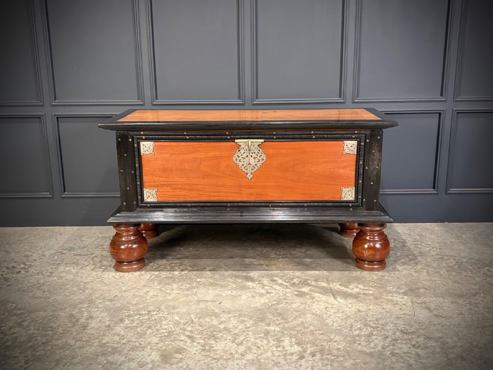 A large Ceylonese camphor wood and ebony storage trunk with an ornate metal escutcheon, side handles, and heavy turned bulbous feet. View IX