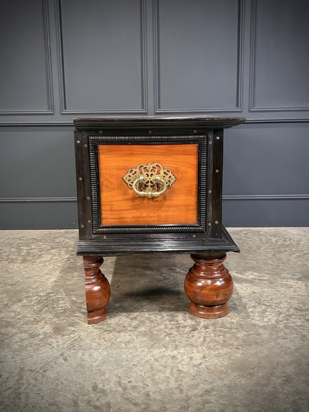A large Ceylonese camphor wood and ebony storage trunk with an ornate metal escutcheon, side handles, and heavy turned bulbous feet. View XIV