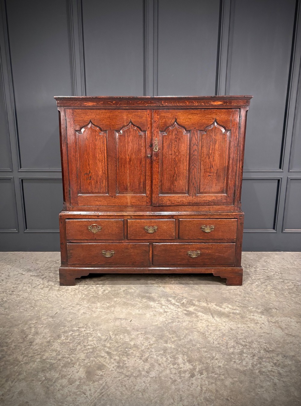 An 18th-century dwarf oak housekeepers cupboard featuring twin doors with pointed arch fielded panels over a base of five drawers. View II
