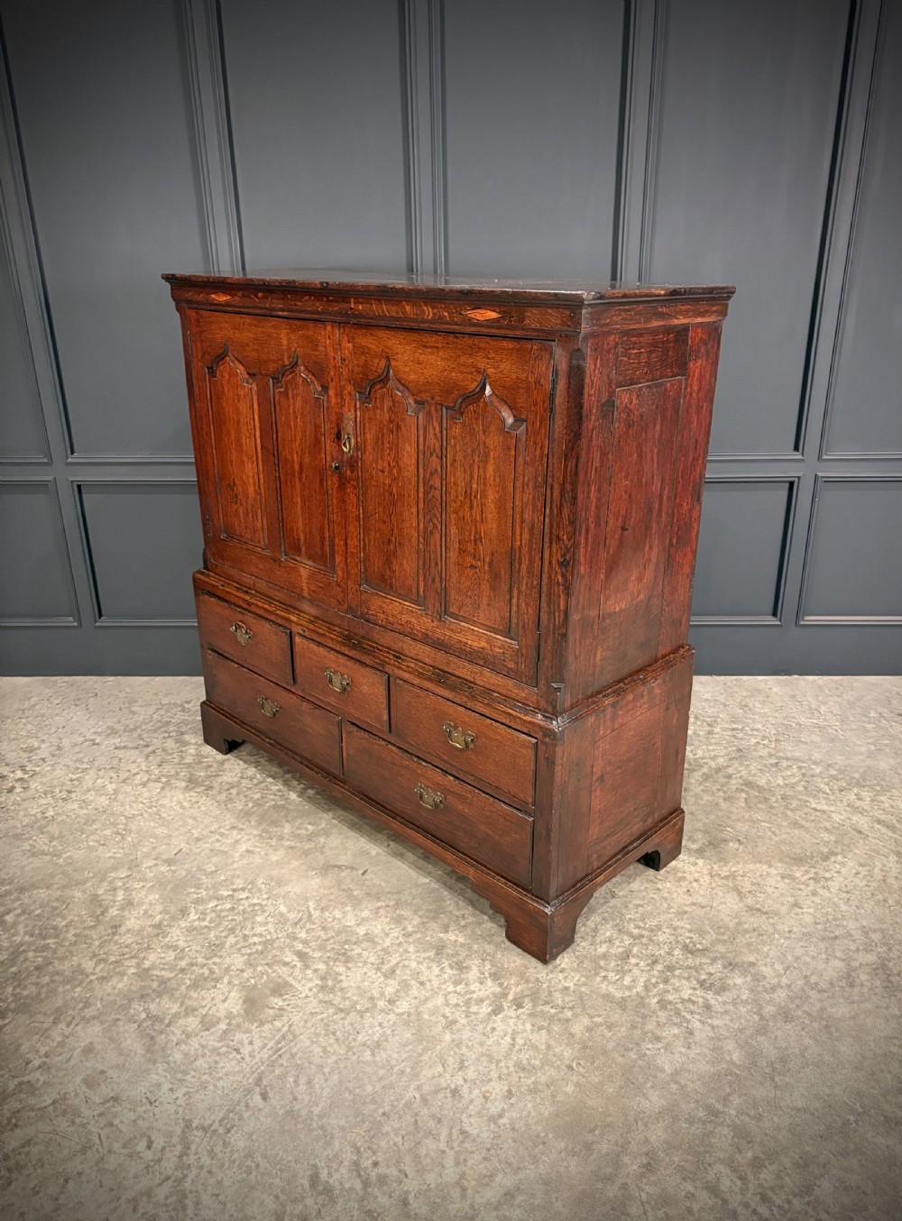 An 18th-century dwarf oak housekeepers cupboard featuring twin doors with pointed arch fielded panels over a base of five drawers. View III