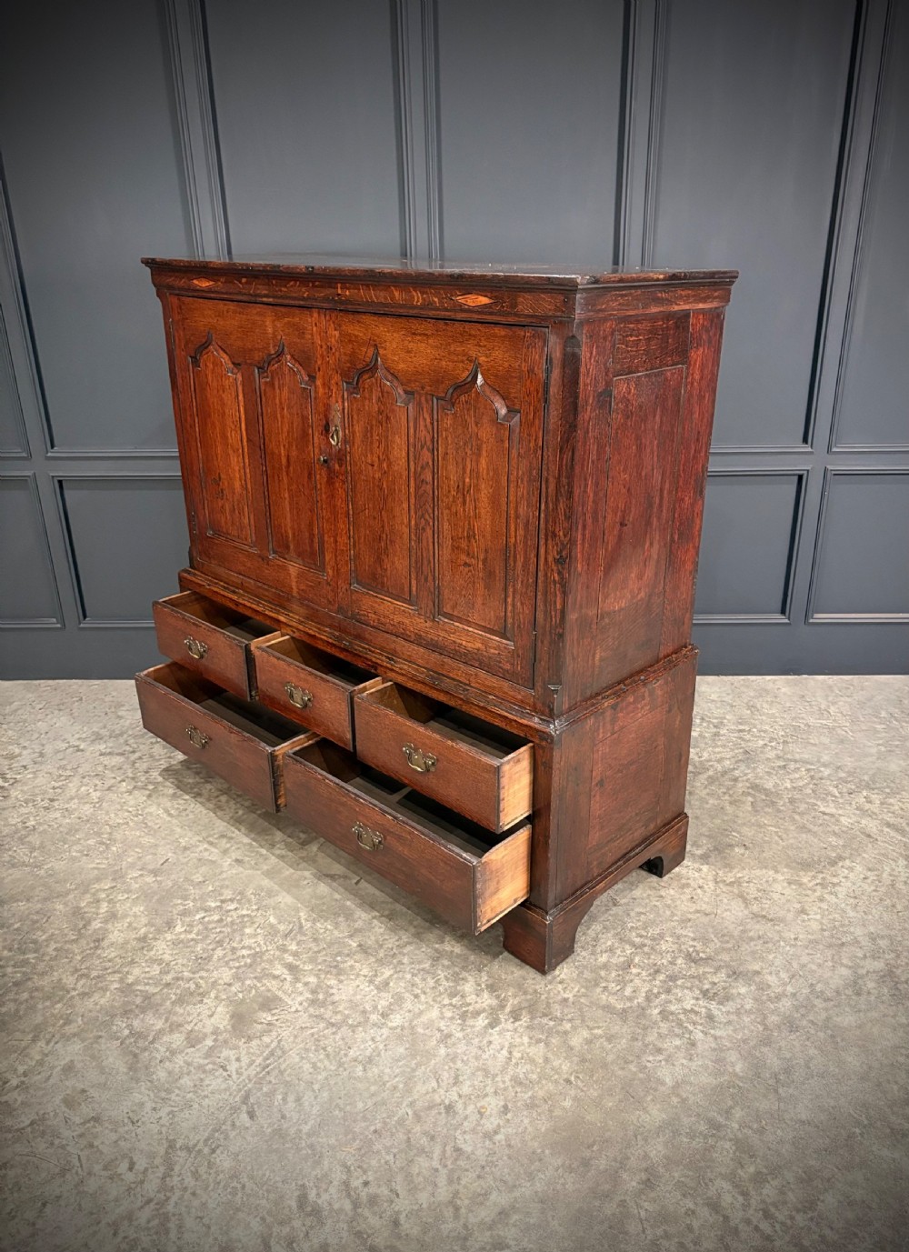 An 18th-century dwarf oak housekeepers cupboard featuring twin doors with pointed arch fielded panels over a base of five drawers. View V