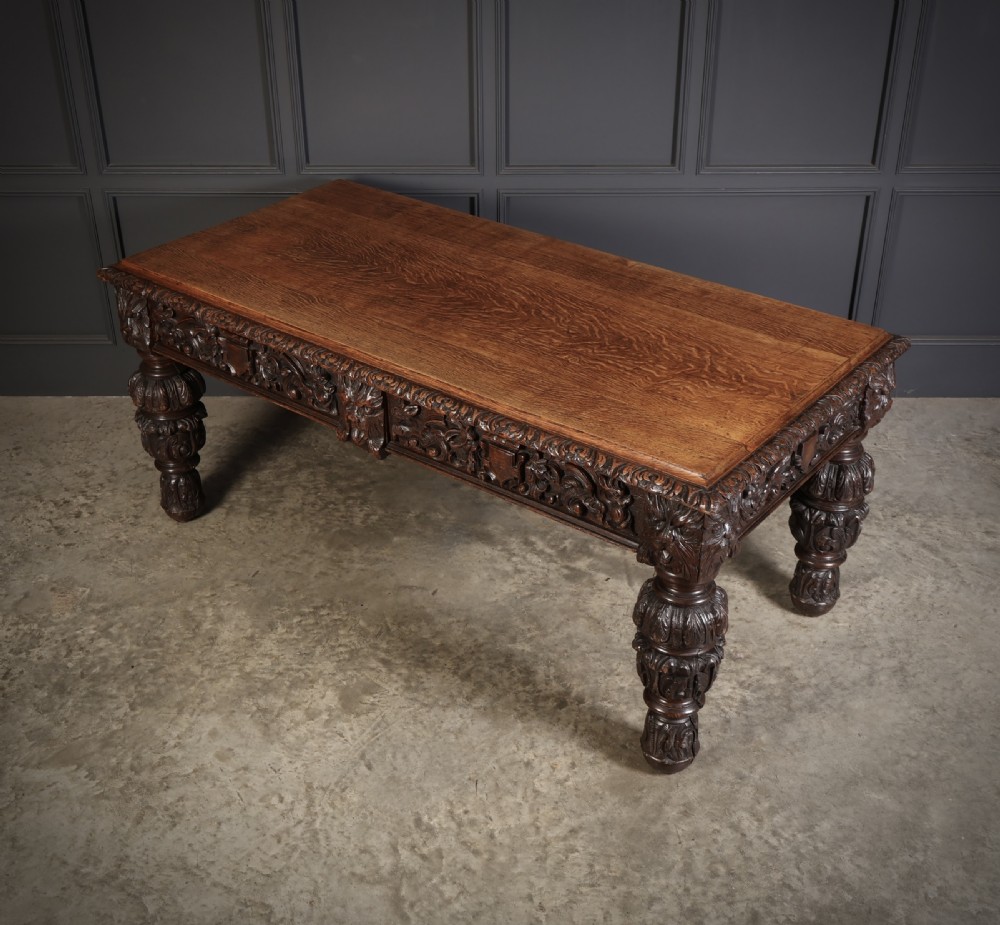 A dark carved oak writing table featuring relief frieze carvings, mask details, and turned legs. View IX