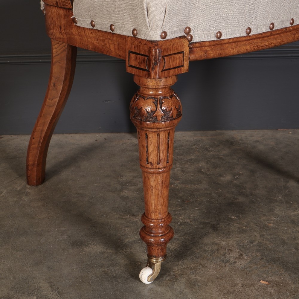 A set of ten Victorian oak dining chairs featuring curved open backs, neutral linen upholstered seats with brass studding, and turned front legs on castors. View V