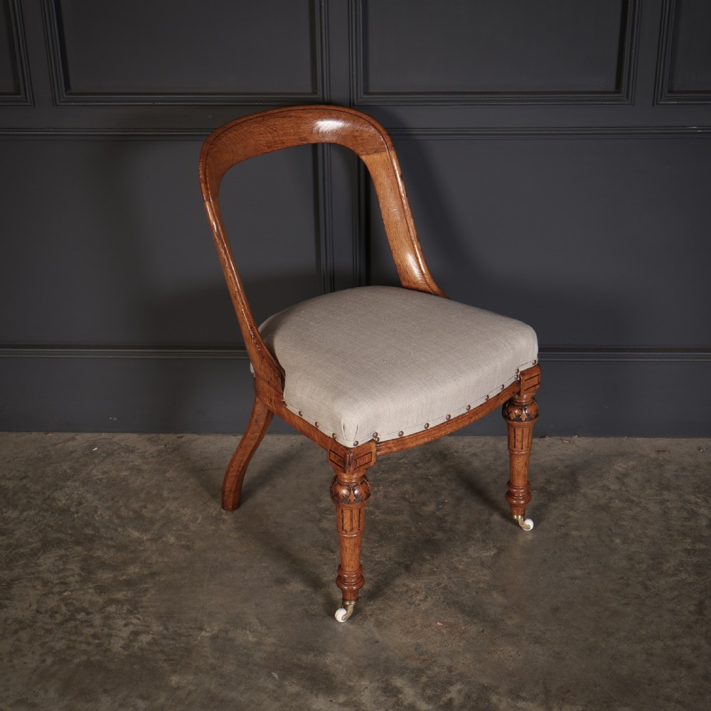 A set of ten Victorian oak dining chairs featuring curved open backs, neutral linen upholstered seats with brass studding, and turned front legs on castors. View II