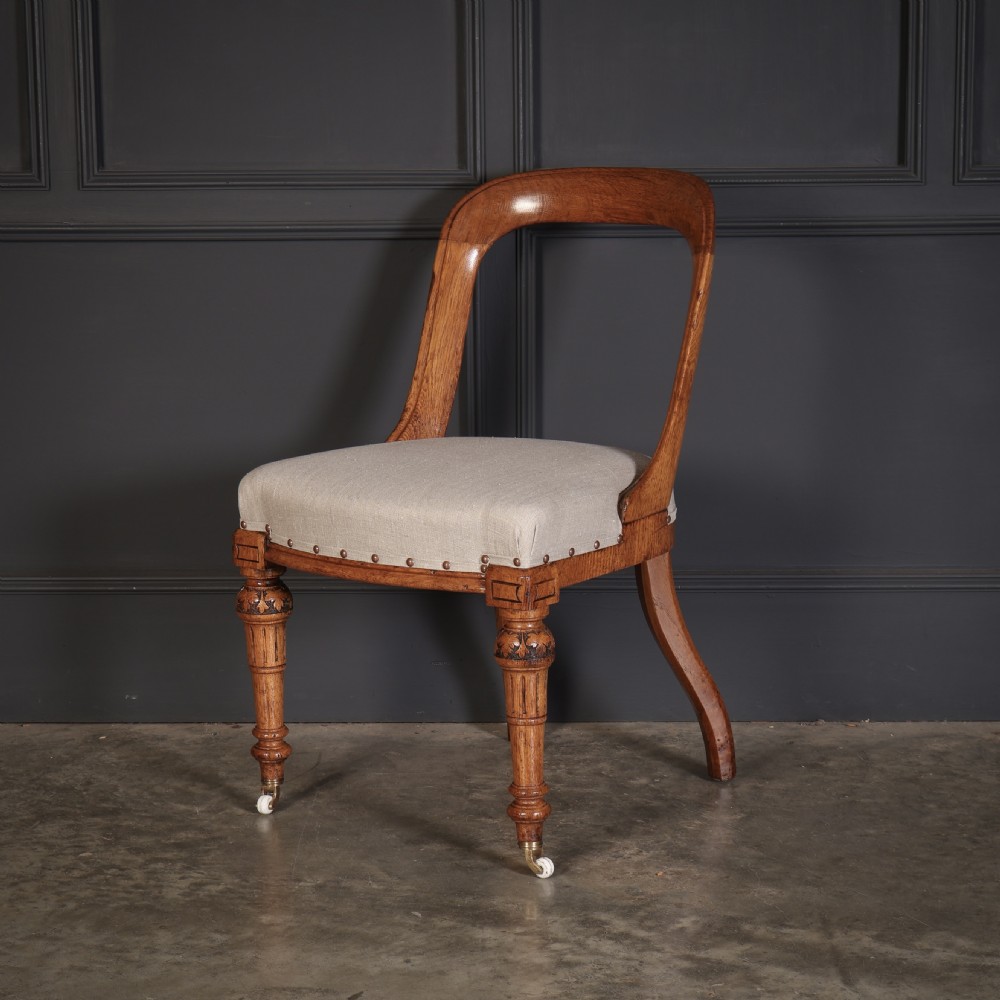 A set of ten Victorian oak dining chairs featuring curved open backs, neutral linen upholstered seats with brass studding, and turned front legs on castors. View VII