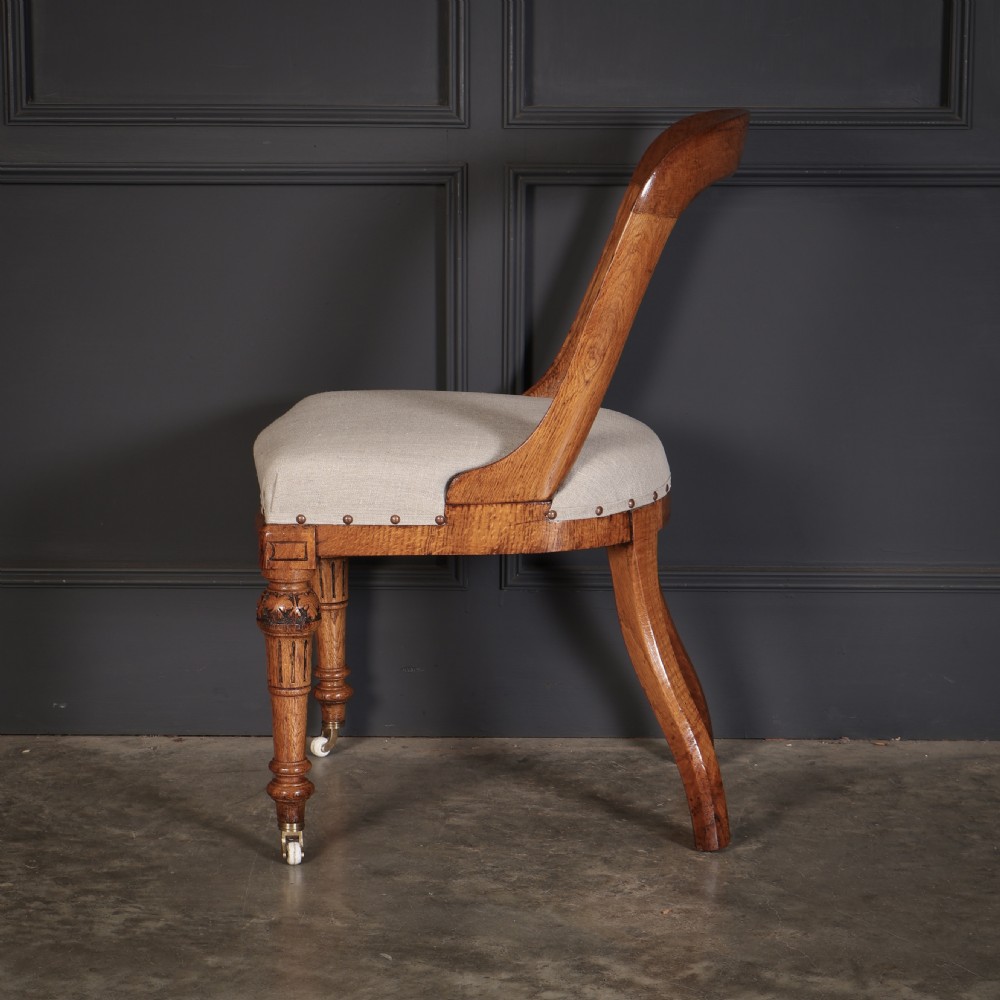A set of ten Victorian oak dining chairs featuring curved open backs, neutral linen upholstered seats with brass studding, and turned front legs on castors. View VIII