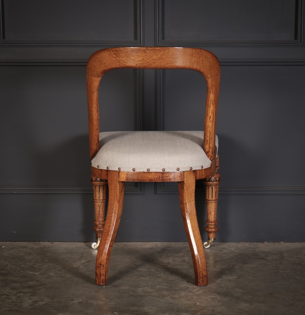 A set of ten Victorian oak dining chairs featuring curved open backs, neutral linen upholstered seats with brass studding, and turned front legs on castors. View IX