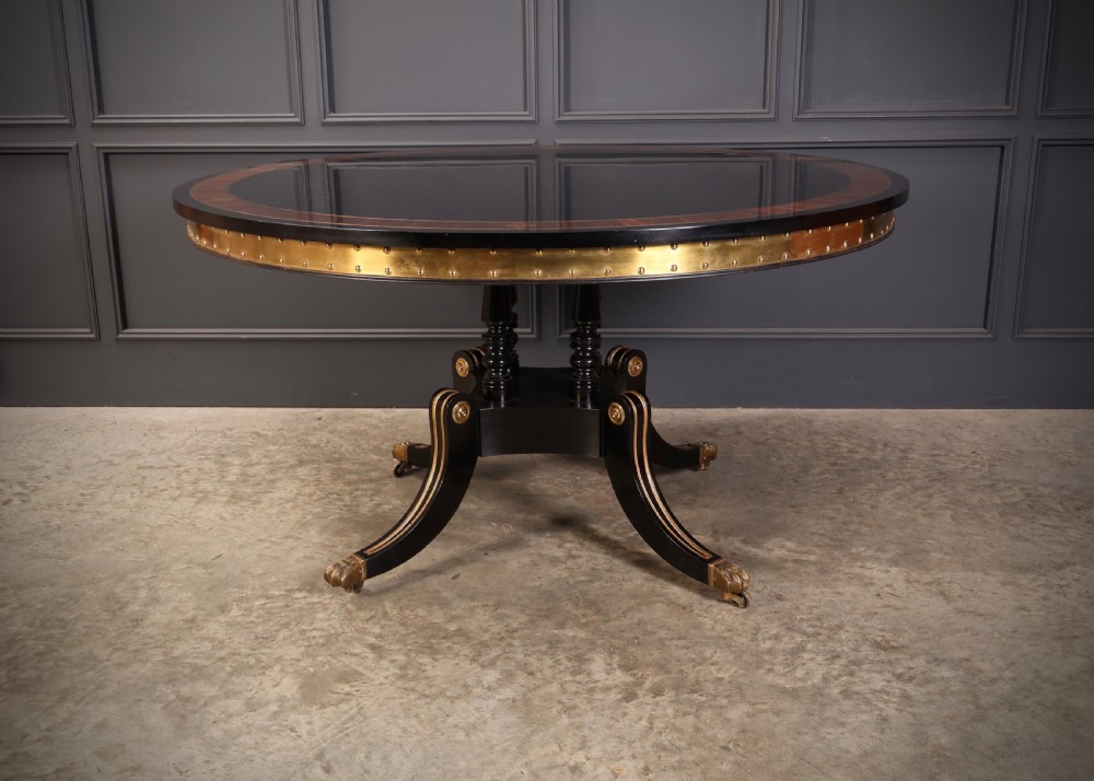 A circular ebonised centre table featuring brass line inlays, a crossbanded top border, a brass apron rim, and a quadruped pedestal base with brass lion paw feet. View IV