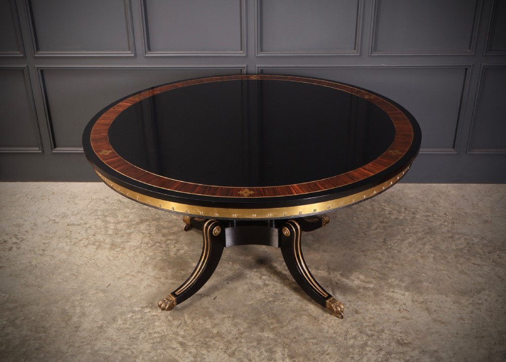 A circular ebonised centre table featuring brass line inlays, a crossbanded top border, a brass apron rim, and a quadruped pedestal base with brass lion paw feet. View II