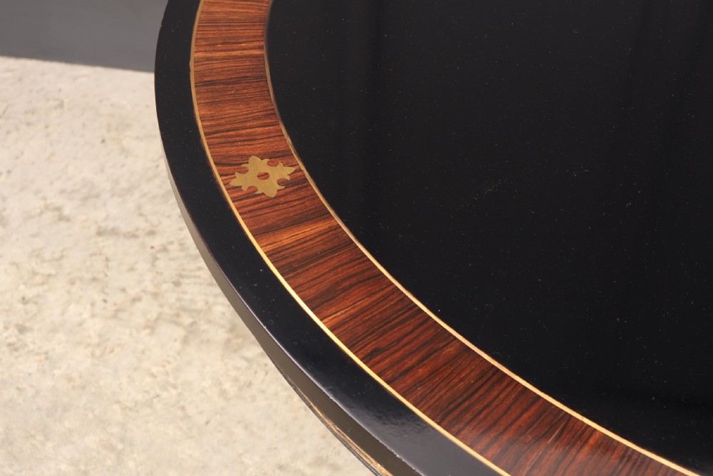 A circular ebonised centre table featuring brass line inlays, a crossbanded top border, a brass apron rim, and a quadruped pedestal base with brass lion paw feet. View V