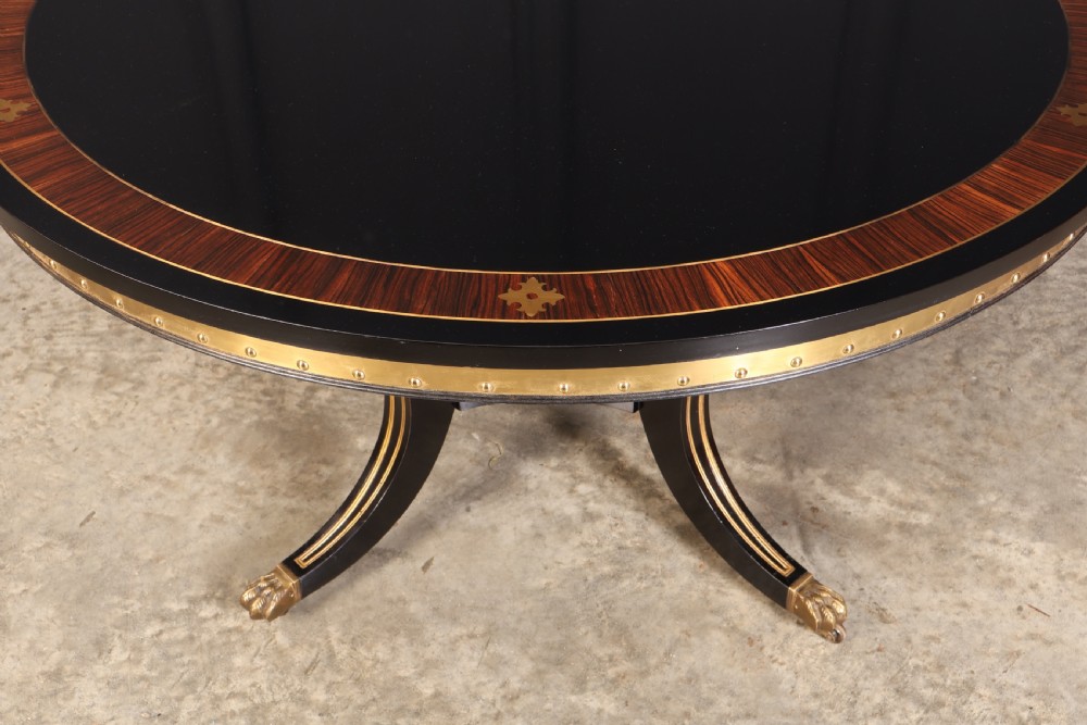 A circular ebonised centre table featuring brass line inlays, a crossbanded top border, a brass apron rim, and a quadruped pedestal base with brass lion paw feet. View VIII