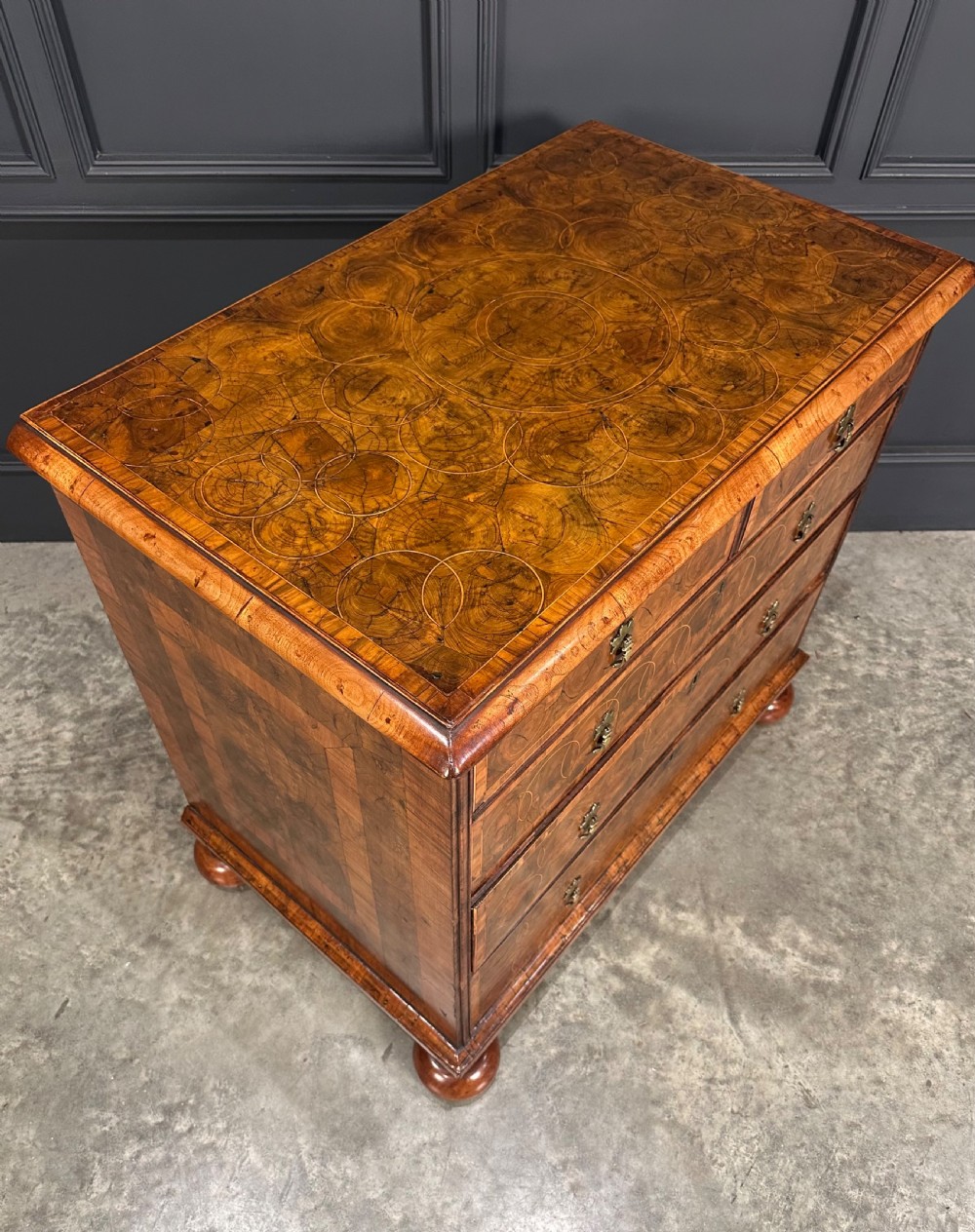 A William and Mary period walnut chest of drawers featuring geometric oyster veneering, brass teardrop handles, and turned bun feet. View II