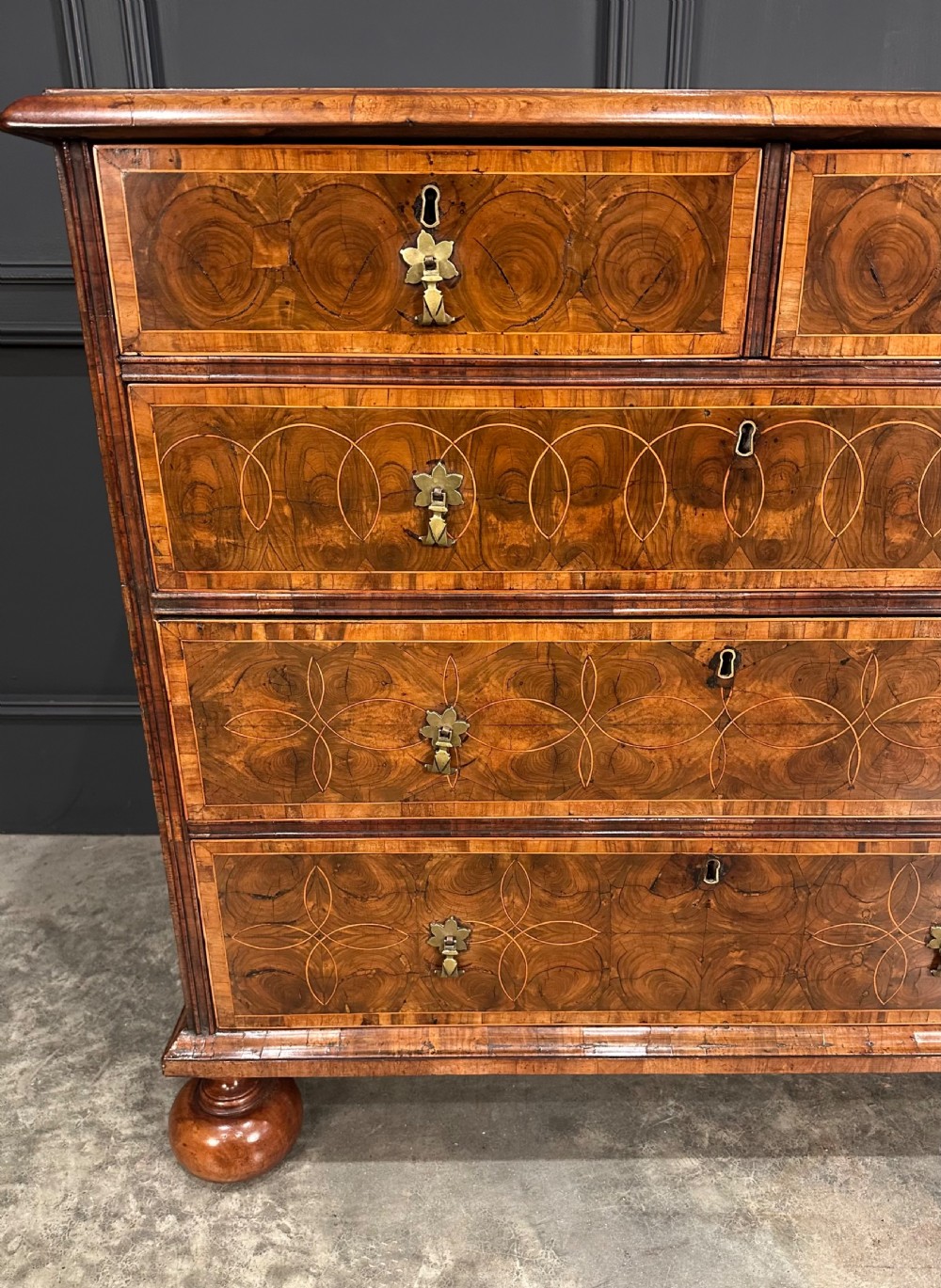 A William and Mary period walnut chest of drawers featuring geometric oyster veneering, brass teardrop handles, and turned bun feet. View V