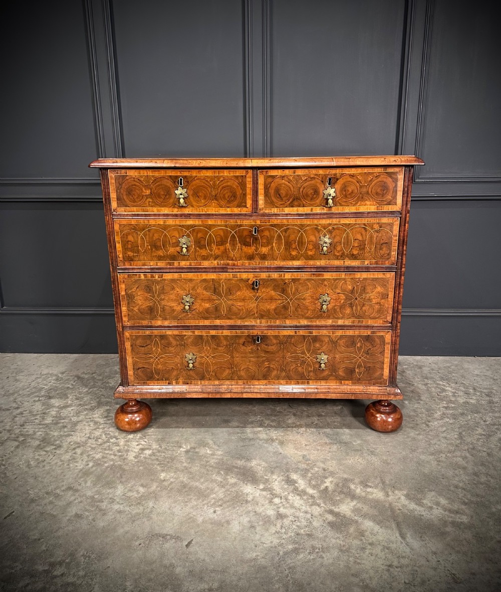 A William and Mary period walnut chest of drawers featuring geometric oyster veneering, brass teardrop handles, and turned bun feet. View VI