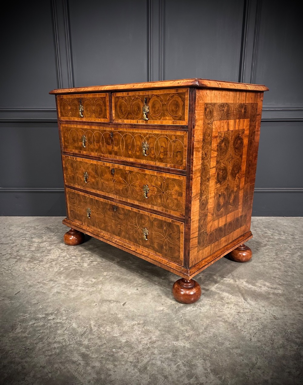A William and Mary period walnut chest of drawers featuring geometric oyster veneering, brass teardrop handles, and turned bun feet. View X