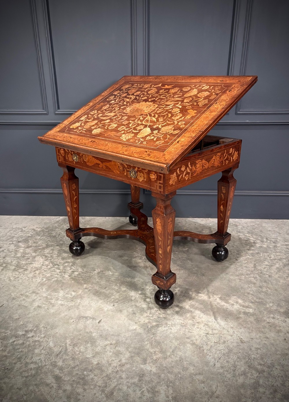 An eighteenth-century Dutch marquetry architects table featuring an adjustable tilted top decorated with floral wood inlays and resting on shaped legs with bun feet.