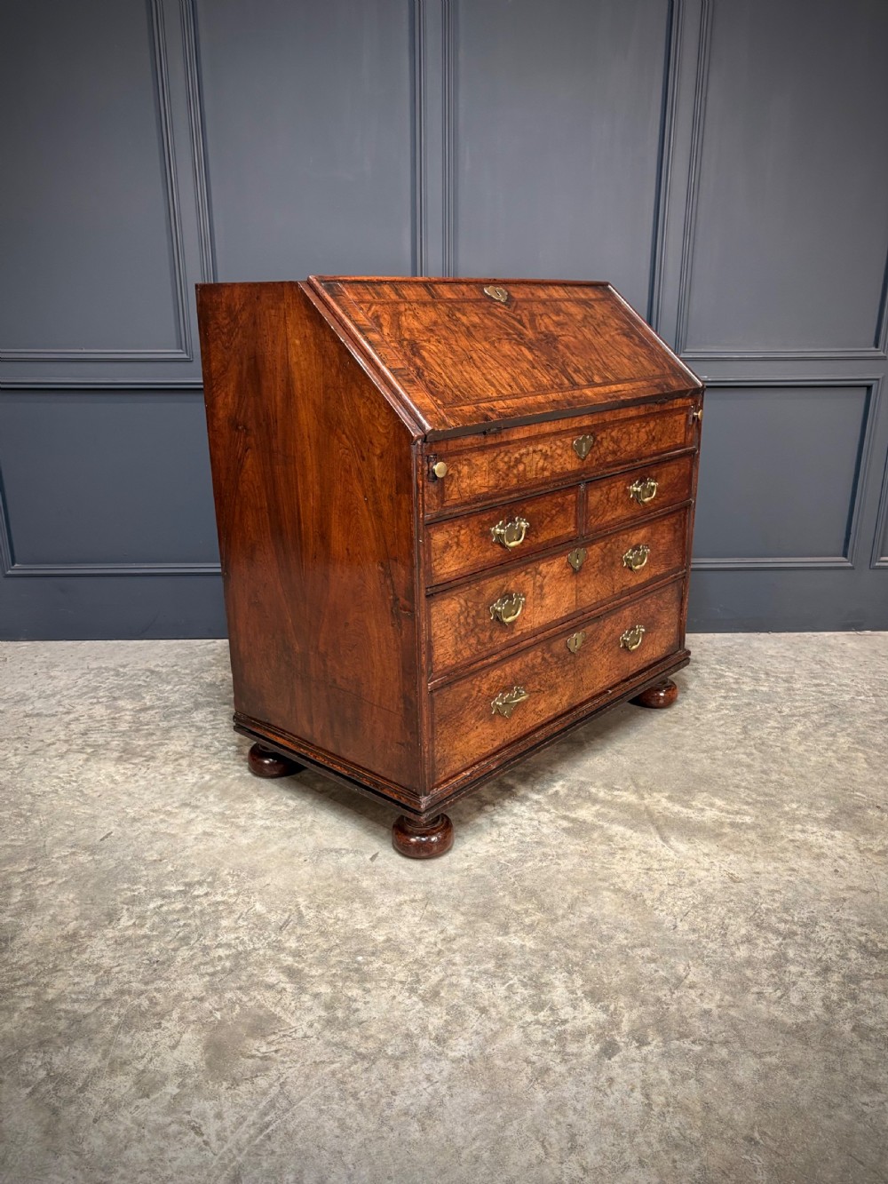 An antique Queen Anne walnut bureau featuring a sloping write-down front above drawers with brass handles, raised on compressed bun feet. View II