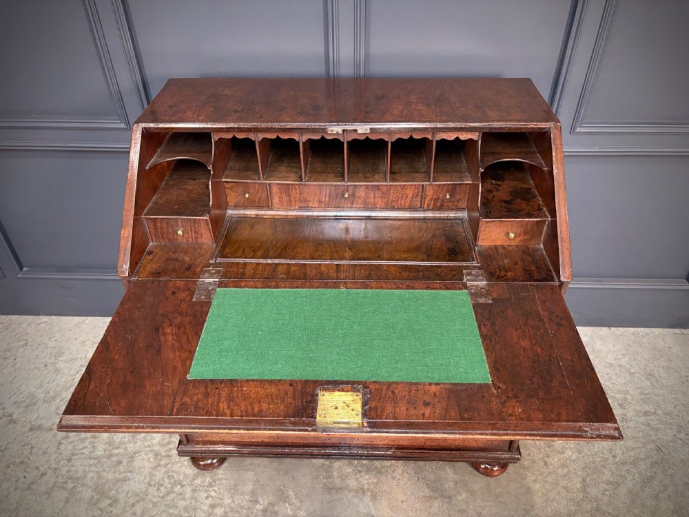 An antique Queen Anne walnut bureau featuring a sloping write-down front above drawers with brass handles, raised on compressed bun feet. View IV