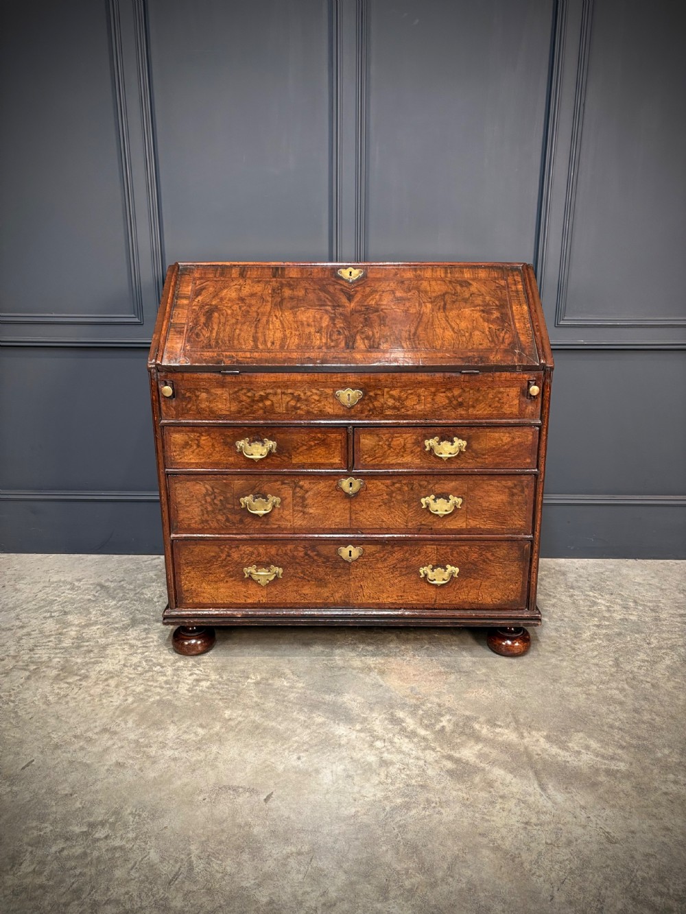 An antique Queen Anne walnut bureau featuring a sloping write-down front above drawers with brass handles, raised on compressed bun feet. View V