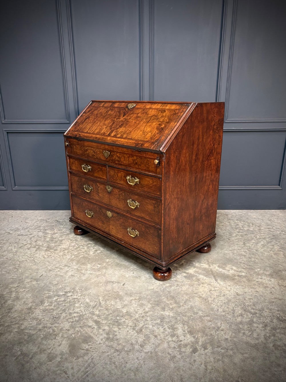 An antique Queen Anne walnut bureau featuring a sloping write-down front above drawers with brass handles, raised on compressed bun feet. View VI