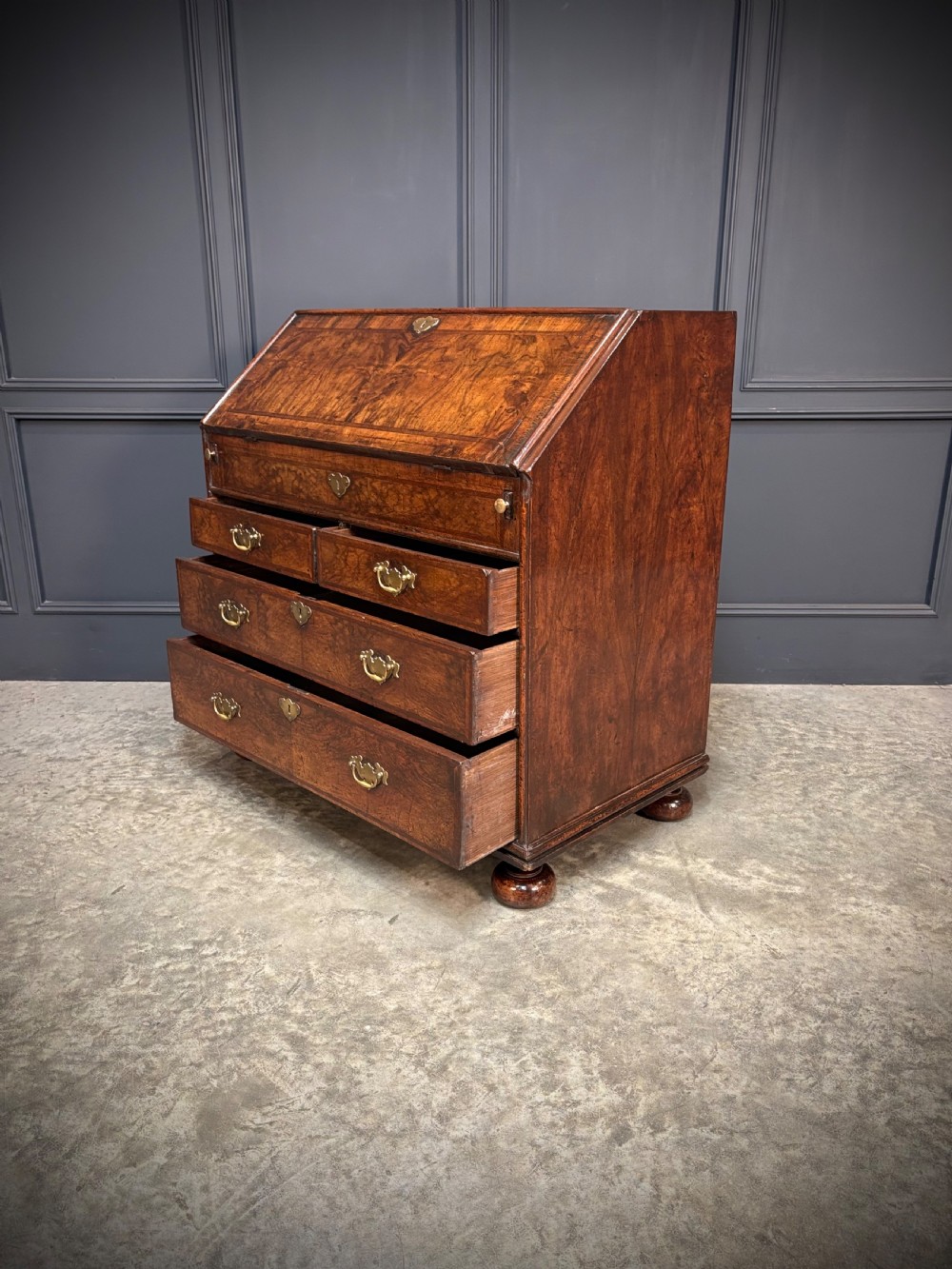 An antique Queen Anne walnut bureau featuring a sloping write-down front above drawers with brass handles, raised on compressed bun feet. View VII